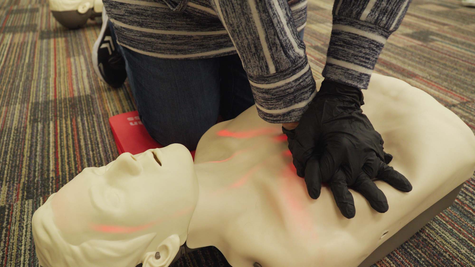 A Red Cross volunteer performs chest compressions on a training dummy.
